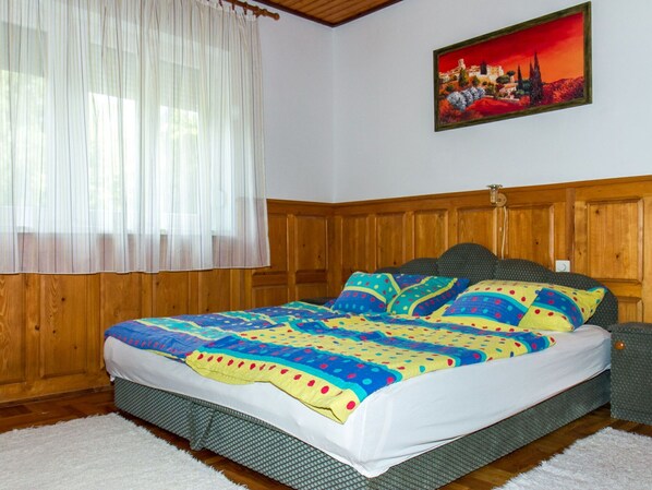 Quarto com cabeceira de madeira, colcha colorida e um quadro na parede.