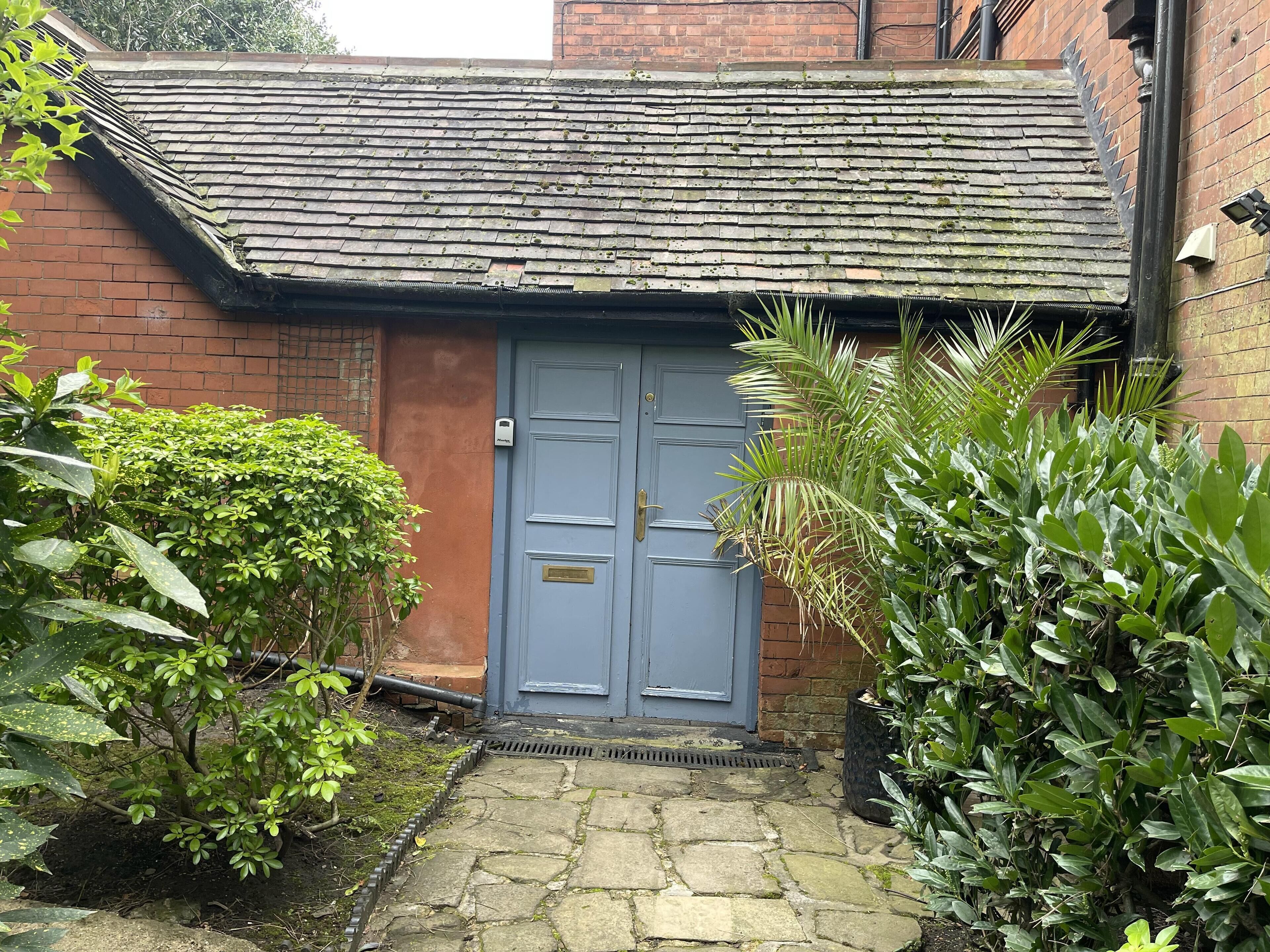 A traditional brick building with a grey door, a tiled roof, and a stone pathway leading to the entrance.