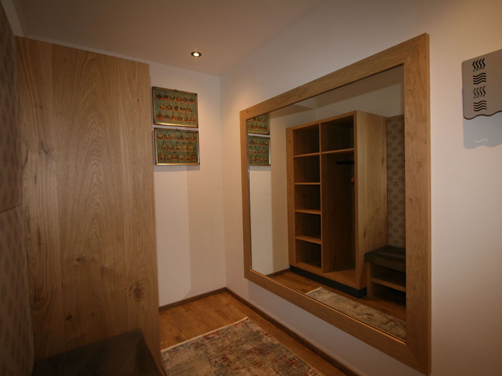 Un couloir avec une porte en bois, un miroir qui reflète une armoire et deux tableaux encadrés accrochés au mur.