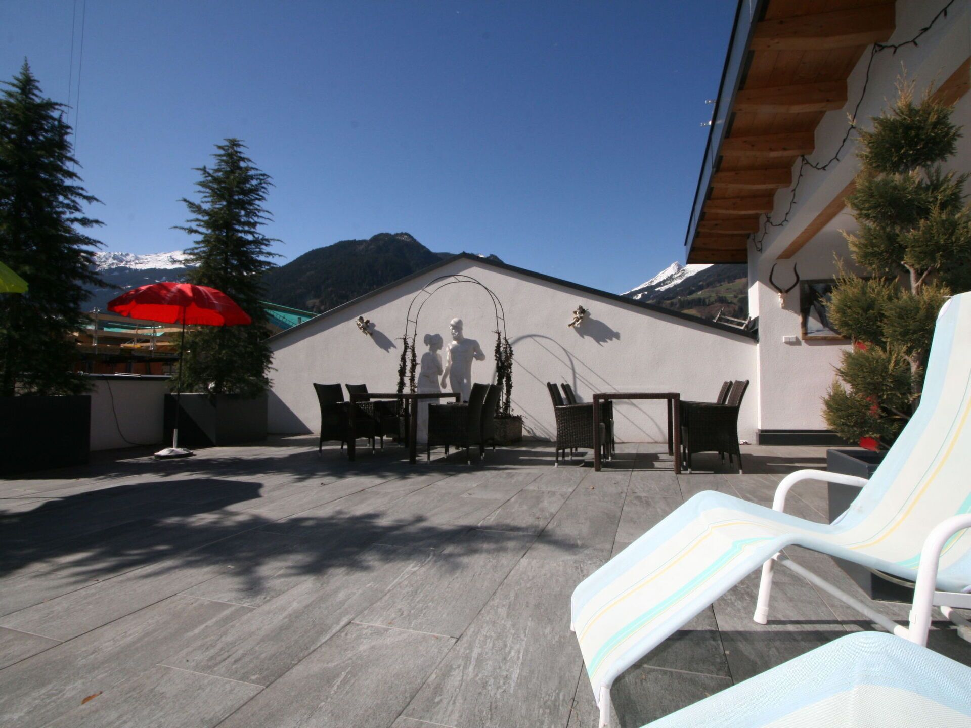 Eine Terrassengruppe mit Tisch und Stühlen, ein roter Sonnenschirm und ein Blick auf die Berge im Hintergrund.