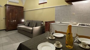 A compact kitchen with a dining area, featuring a sofa, a dining table set for two, and a built-in stove.