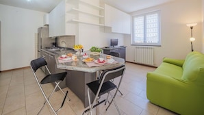 A modern kitchen with a central island, a dining area with chairs, a green sofa, and a window with patterned curtains. - Nice apartment for 4 guests with A/C, WIFI, TV and balcony (Sestri Levante)