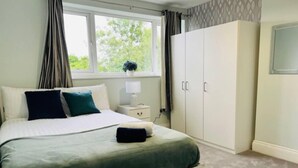 A bedroom with a bed, a nightstand, a wardrobe, and a window with curtains. - 4 Bed House - Sleeps 9 - Garden - Parking - Wifi (Birmingham)