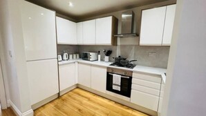 A compact kitchen with white cabinets, a microwave, a kettle, and a stove. - 4 Bed House - Sleeps 9 - Garden - Parking - Wifi (Birmingham)