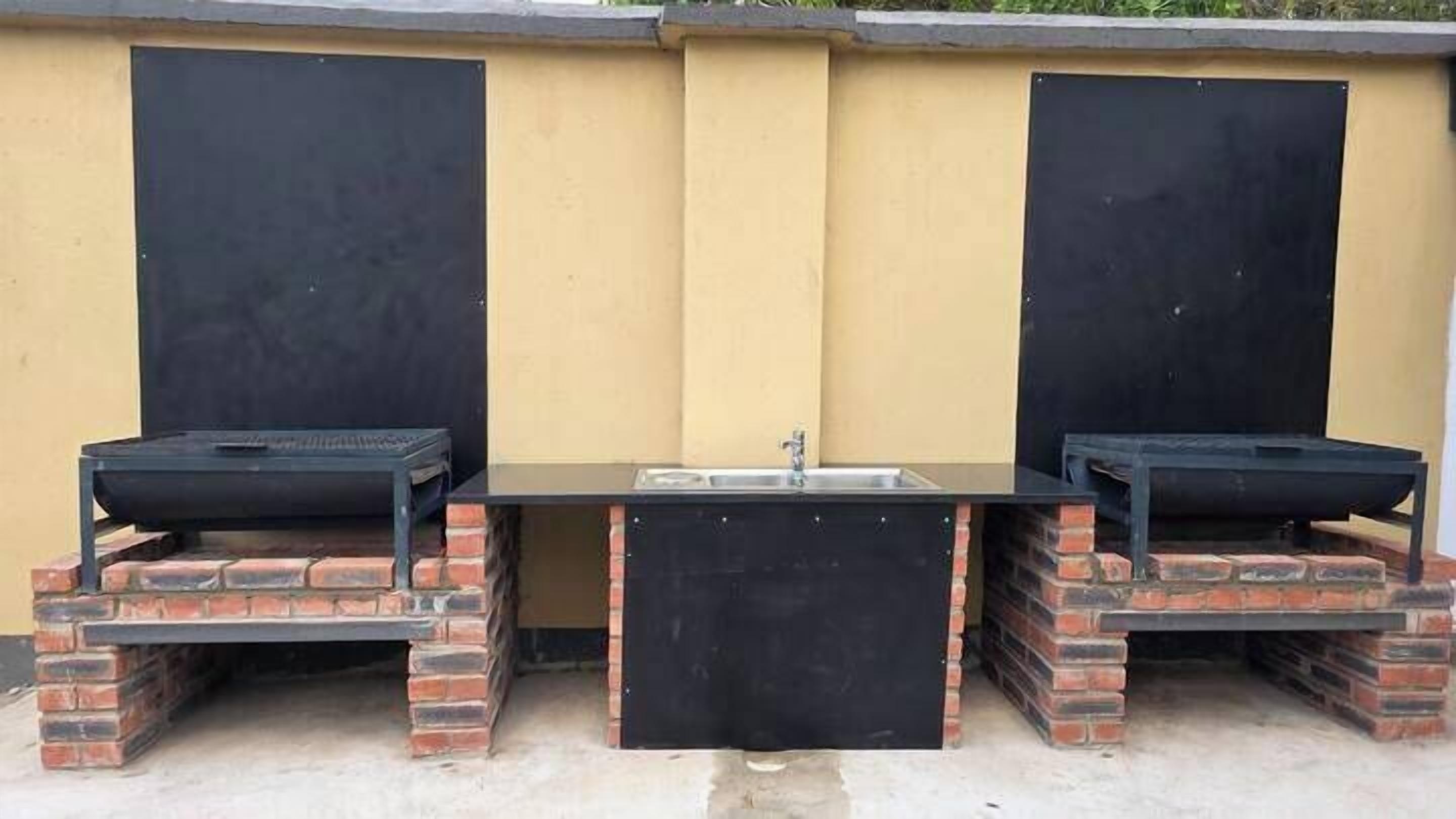 An outdoor barbecue area with two brick-built barbecue grills and a central sink.