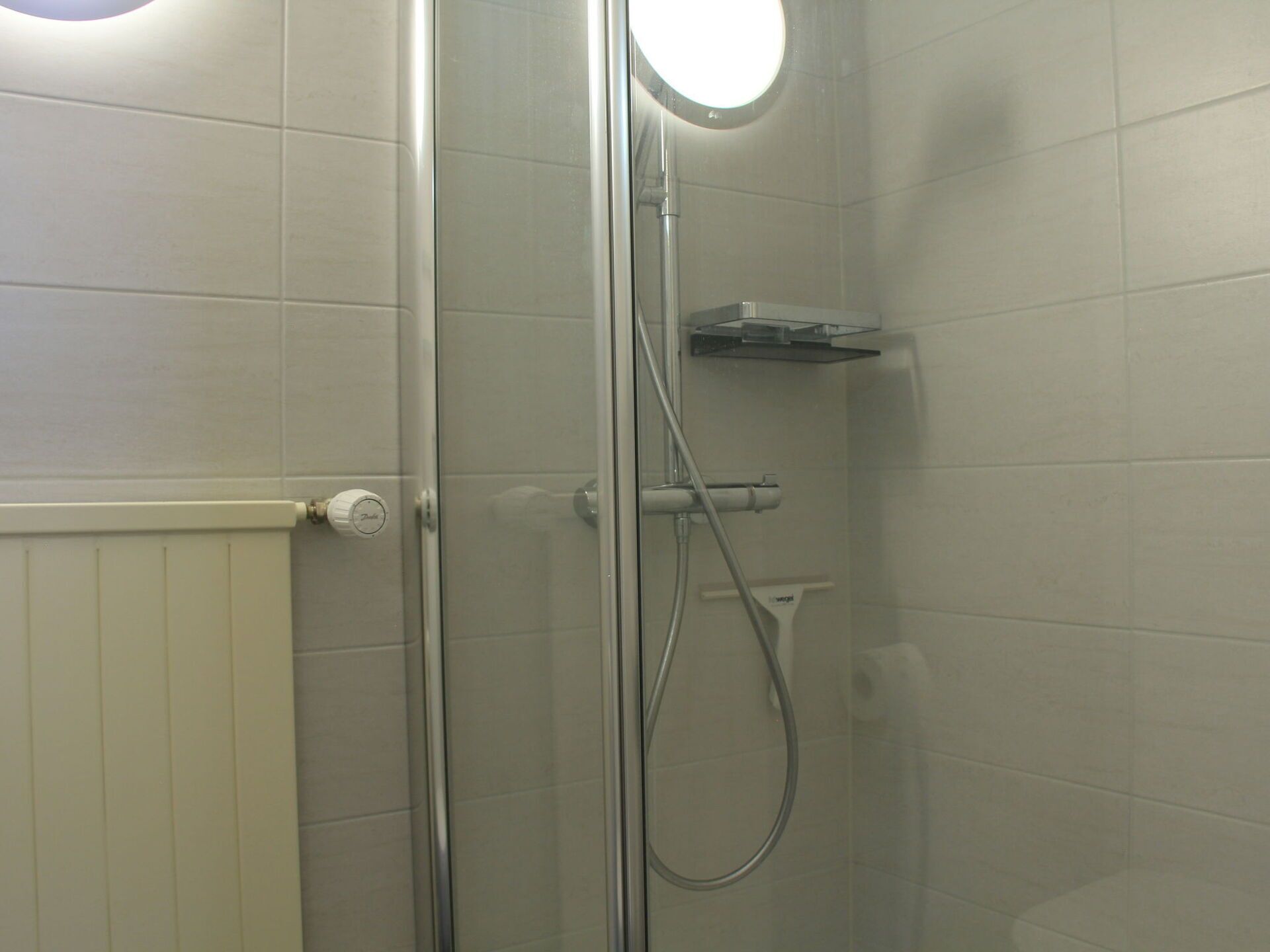 Ducha envuelta en vidrio con cabezal de ducha de mano y panel de control en la pared.