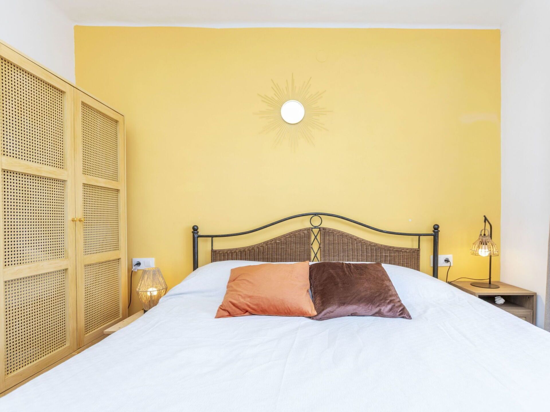 A bed with two pillows, a wall clock, and a nightstand with a lamp.