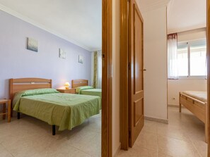 A room with two beds, a wooden door, and a window with curtains. - Lovely apartment for 6 guests with pool, A/C, WIFI, TV and terrace (La Pineda)