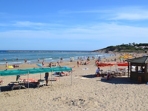 A beach with sun loungers, umbrellas, and a small building, likely a snack or rest area.
