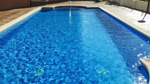 Een rechthoekig zwembad met helderblauw water, omgeven door een betegeld zonnedek.