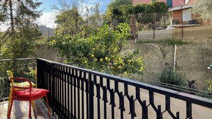 A balcony with a red chair, a black railing, and a view of a building with green shutters and a satellite dish. - Cosy apartment for 6 guests with A/C, WIFI, TV and balcony (Imperia)