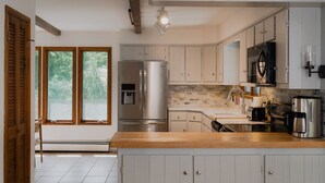A modern kitchen with a large island, stainless steel appliances, and a view of greenery through the windows.