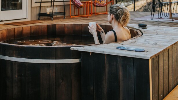 A hot tub area with a wooden deck, outdoor seating, and a glass-enclosed structure.