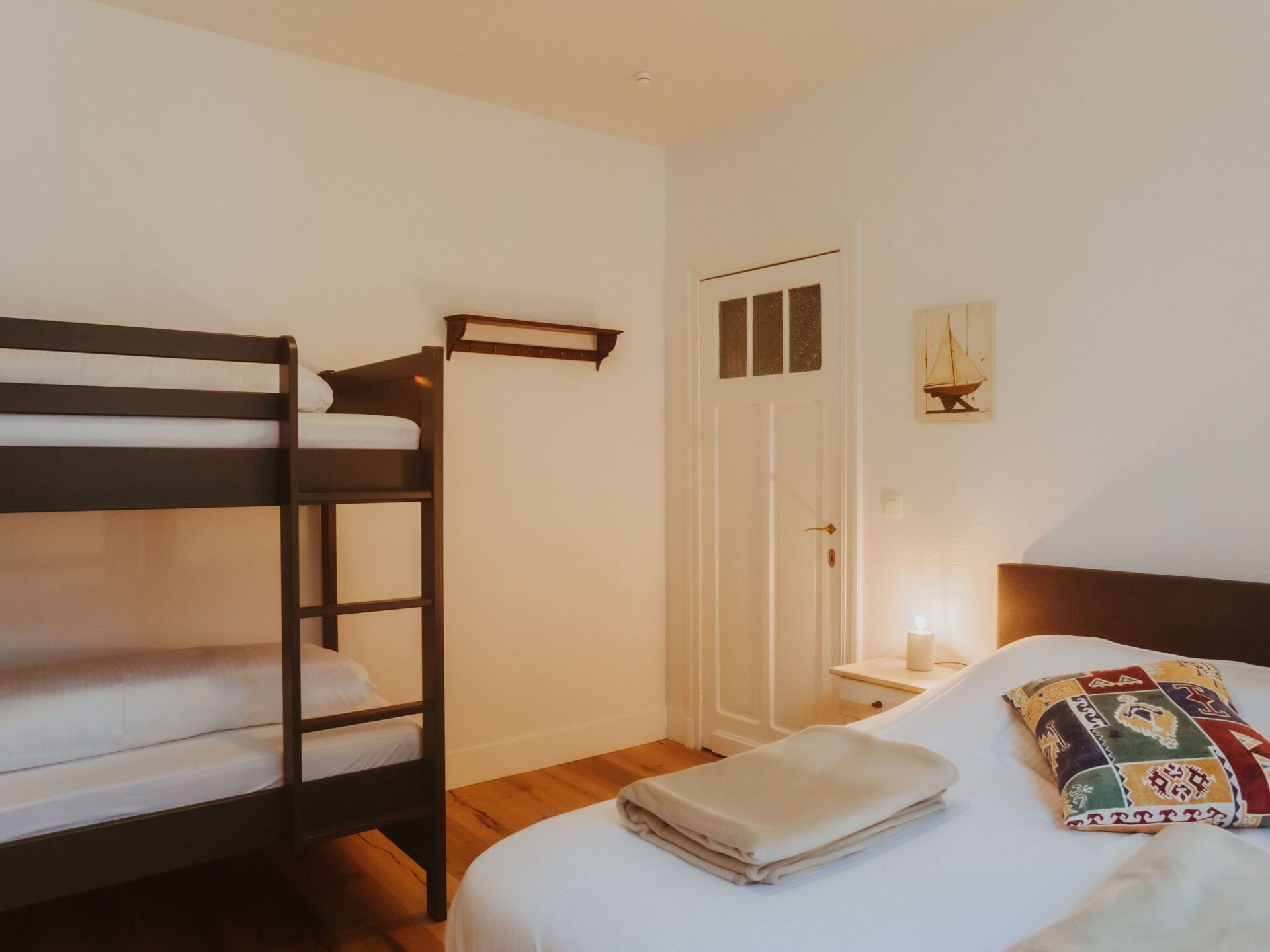 Een kamer met een stapelbed, een nachtkastje met een kaars, en een bed met een kleurrijk kussen.