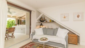 A cozy living room with a sofa, a small round table, and a patterned rug. There is a staircase leading to an upper level with shelves and decorative items.