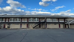 Un motel con una escalera central, varias habitaciones y un estacionamiento.