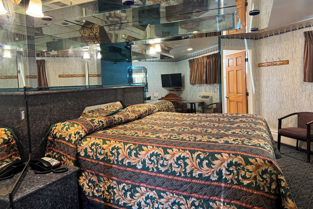 A hotel room with a large bed, a desk, a chair, a telephone, a television, and a mirror.