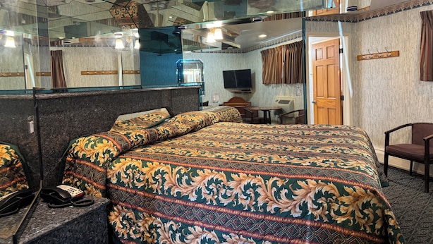 Habitación de hotel con una cama grande, un escritorio, una silla, un teléfono, un televisor y un espejo.