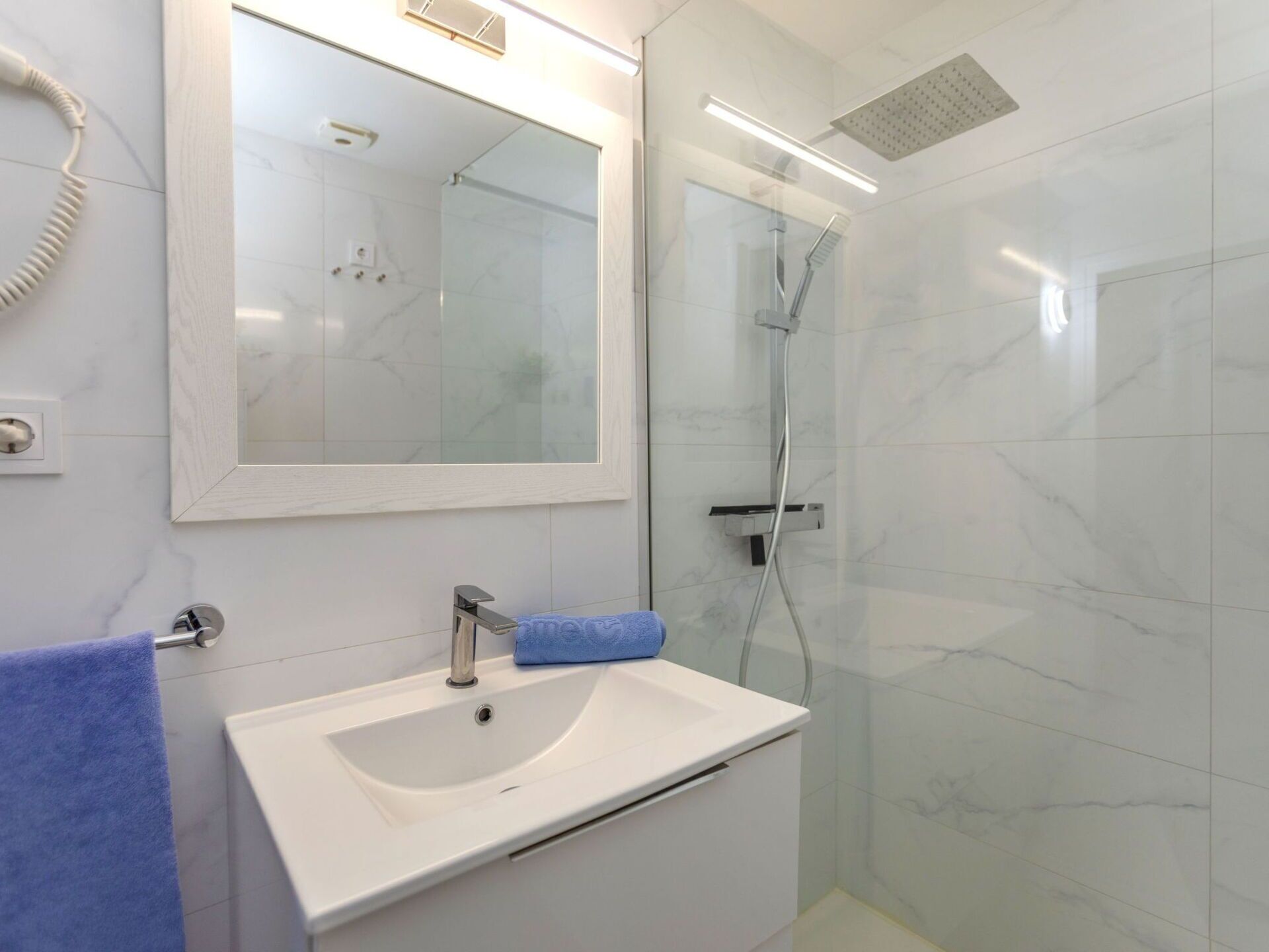 A bathroom with a white sink, a mirror, a glass-enclosed shower, and a towel rack.