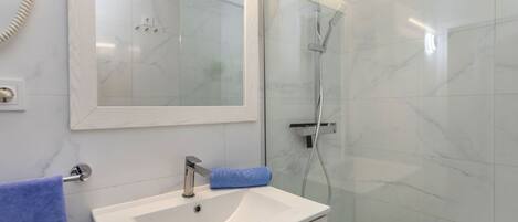 A bathroom with a white sink, a mirror, a glass-enclosed shower, and a towel rack.