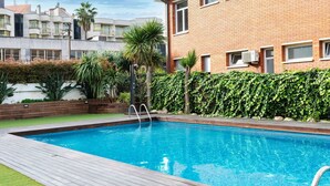A swimming pool with a wooden deck, surrounded by a brick building and lush greenery. - Nice apartment for 4 guests with A/C, WIFI, pool, TV and balcony (Lloret De Mar)