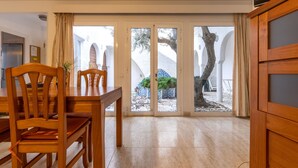 Ein Essbereich mit einem Holztisch und Stühlen, einem Fernseher und Blick auf einen Innenhof mit Baum und einer Kachelwand.