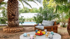 A round table with a stone base, surrounded by a wooden bench and a cushioned chair, with a fruit bowl and cups on the table. - Beautiful private villa for 6 people with WIFI, private pool, A/C, TV and patio (Miami Platja)