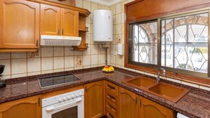 A kitchen with wooden cabinets, a built-in stove, a sink, and a window with decorative iron bars. - Stunning private villa for 6 guests with private pool, A/C, WIFI, TV and terrace (Miami Platja)