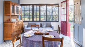 A dining area with a round table set for four, a wooden cabinet with glass doors, and a view through large windows. - Wonderful private villa for 5 guests with WIFI, TV, terrace and pets allowed (Mimizan)
