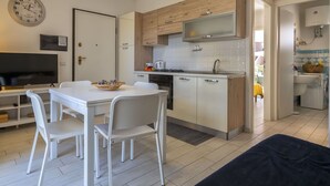Una cocina moderna con armarios blancos, un microondas y un lavamanos. Hay una mesa de comedor con sillas y un televisor en la esquina.