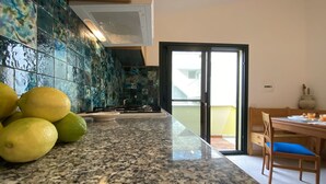 Une cuisine dotée de plans de travail en granit, d’un évier et d’une cuisinière. On peut voir des citrons sur le plan de travail. Un coin repas avec une table et des chaises est visible à travers une porte vitrée.