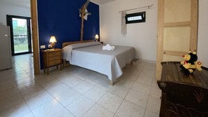 A bedroom with a bed, two bedside tables with lamps, a window with curtains, and a wooden dresser with a plush toy.