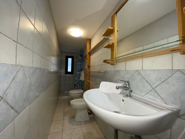 A bathroom with a white sink, two toilets, a shower, and a window.