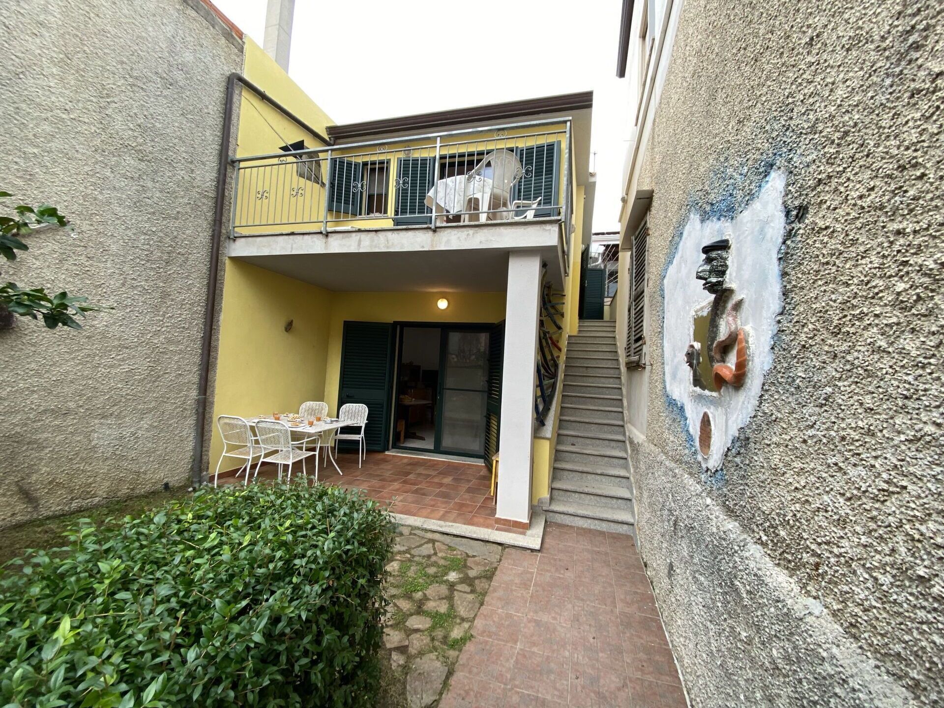 Une petite cour comprenant un espace repas, un escalier et une fresque murale.