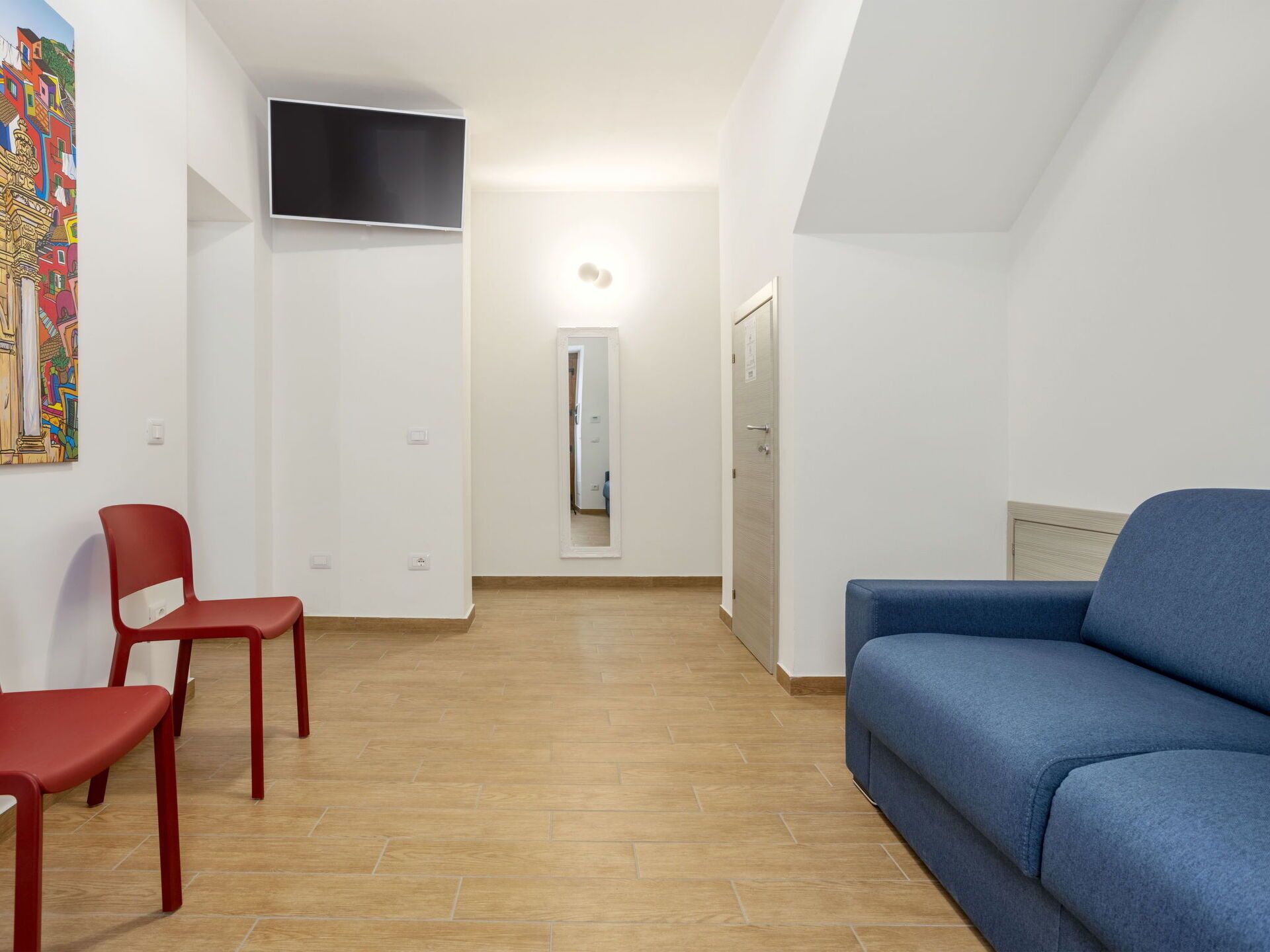 A modern living room with a blue sofa, a red chair, and a television mounted on the wall.