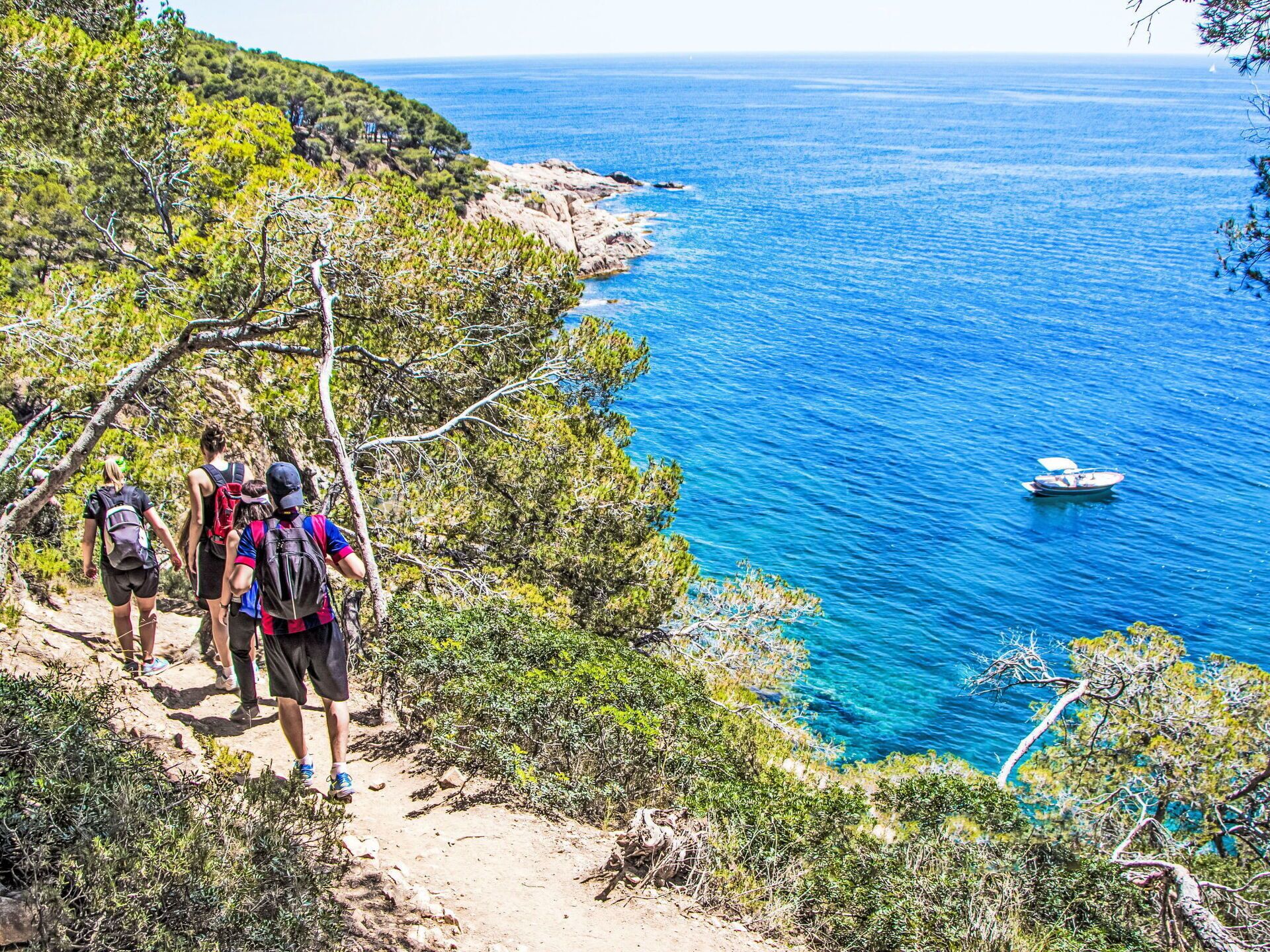 Un sentier de randonnée le long de la côte, avec des randonneurs et un bateau en arrière-plan.