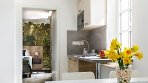 Een moderne keuken met een eethoek, uitzicht op een bos door een deur, en een vaas met bloemen op de tafel.
