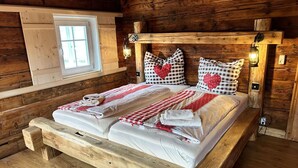 A wooden cabin-style bedroom with a bed, checkered bedding, heart-shaped pillows, and wall-mounted lights.