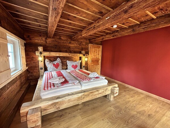 A wooden cabin bedroom with a bed, two bedside lamps, and a red wall.