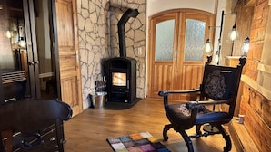 A cozy room with a stone wall, a fireplace, wooden furniture, and a colorful rug.