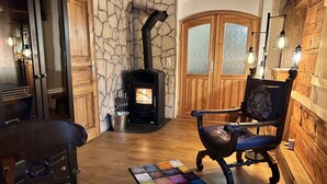 A cozy room with a stone wall, a fireplace, wooden furniture, and a colorful rug.
