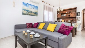 A modern living room with a grey sofa, colorful cushions, a coffee table with pastries, and a painting of a beach scene.