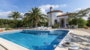 A swimming pool with lounge chairs, a stone building with a tiled roof, and palm trees.