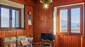Ein Holzinterieur mit einem runden Tisch, Stühlen, einer Uhr und Blick auf Berge durch große Fenster.