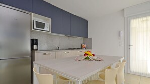 A modern kitchen with a stainless steel refrigerator, a microwave, and a coffee maker. There is a dining table with chairs and a fruit bowl on the table. - Nice apartment for 8 people with A/C, WIFI, TV, balcony and pets allowed (Lignano Sabbiadoro)