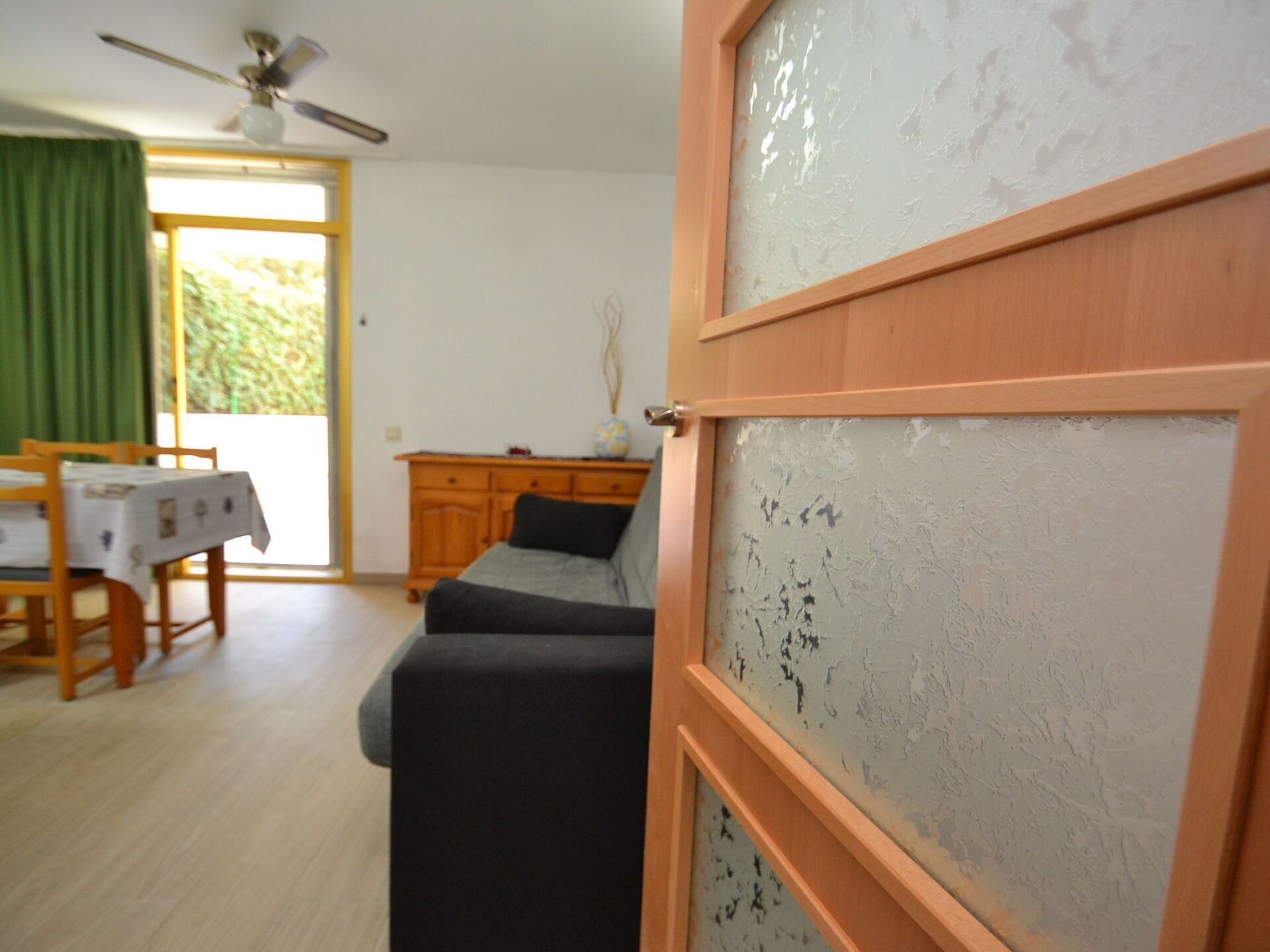 A room with a wooden cabinet, a sofa, a dining table with chairs, and a ceiling fan.