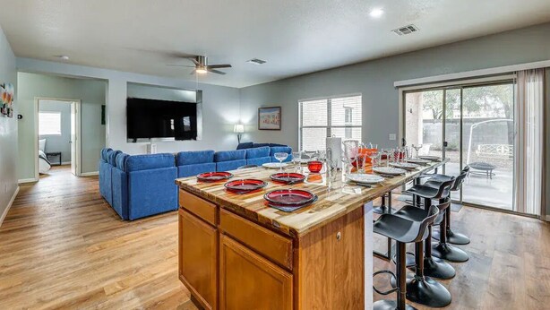 A spacious living area with a blue sofa, a wooden island bar with stools, and a large TV mounted on the wall. - Mesa Vacation Home - Sleeps 12 - Close to Golf Courses and SO MUCH MORE! (Mesa)