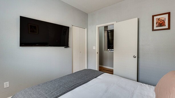 Ein Schlafzimmer mit Bett, einem an der Wand befestigten Fernseher, einem Kleiderschrank und einer Tür zu einem Badezimmer.