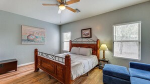 A bedroom with a wooden bed, a ceiling fan, a nightstand with a lamp, a blue chair, and two windows with blinds. - Mesa Vacation Home - Sleeps 12 - Close to Golf Courses and SO MUCH MORE! (Mesa)
