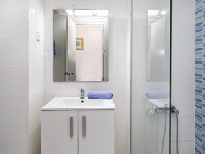 Un baño con lavamanos blanco, espejo y cabina de ducha con mampara de vidrio.